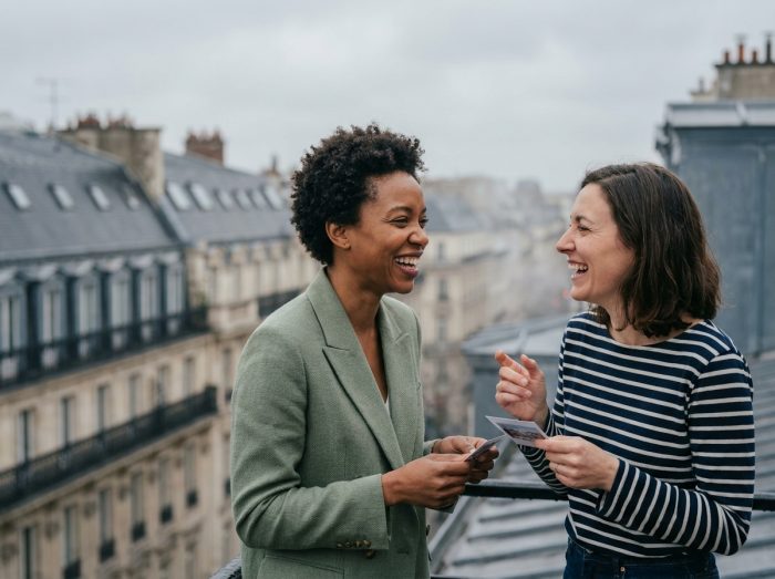 Deux collègues souriantes participant à un jeu de team building en plein air sur une terrasse avec les toits de Paris en arrière-plan
